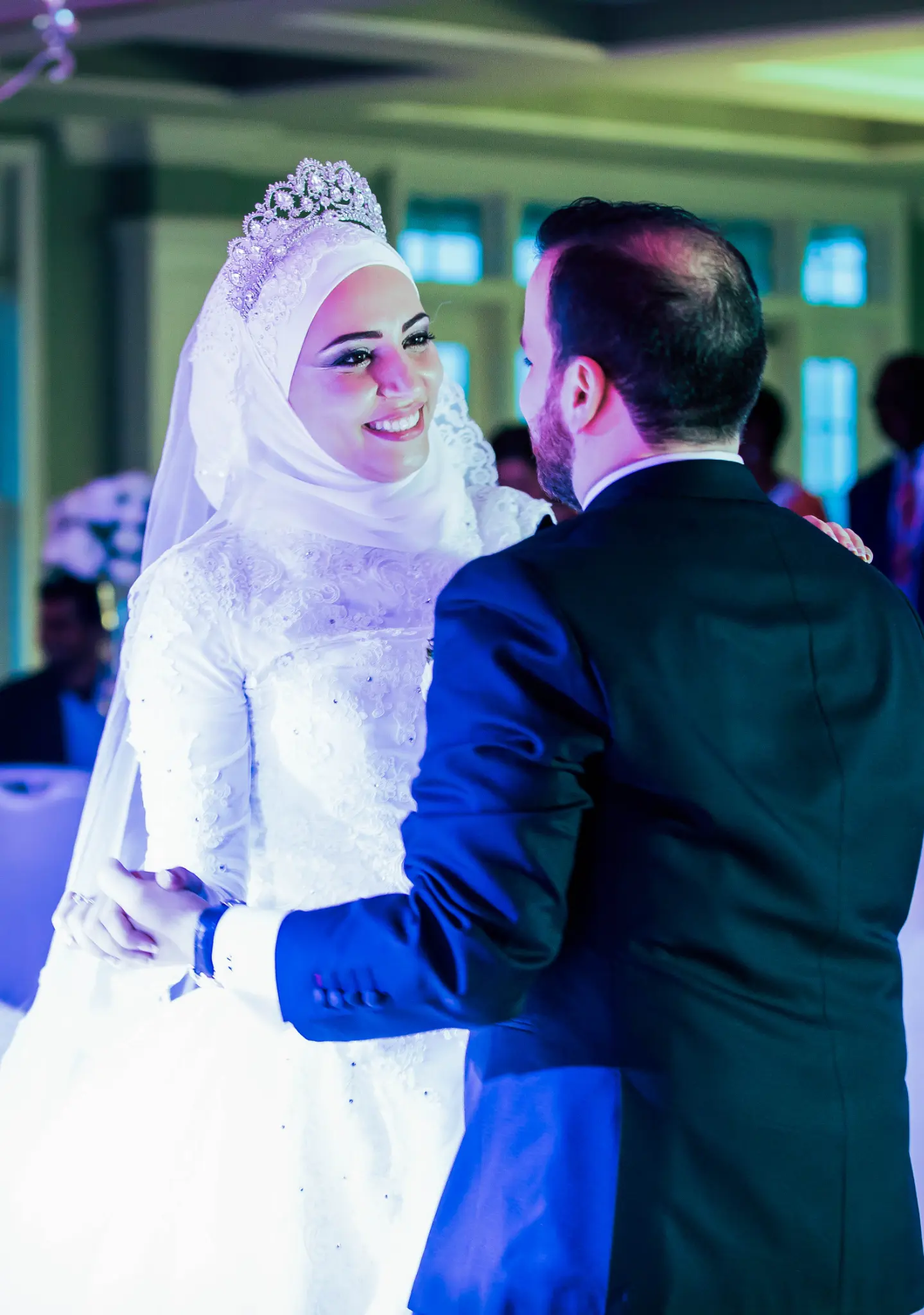 Muslim bride in hijab and tiara crown smiling during first dance with groom